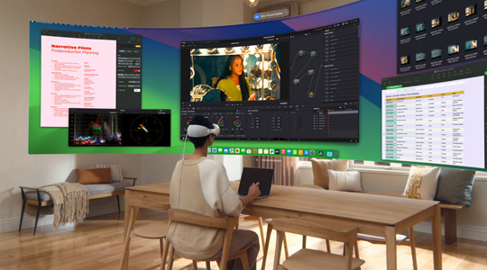 一个佩戴 Apple Vision Pro 的人坐在桌前，桌上有一台打开的 13 英寸 MacBook Pro，屏幕内容显示在一个横跨房间的超宽曲面屏上。