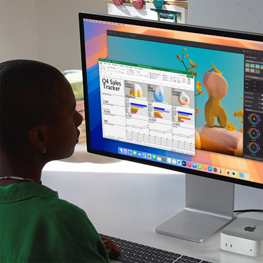 一名女子坐在桌前，正在使用 Mac 处理 Excel 电子表格，内容为第四季度销售追踪表。Excel 电子表格窗口后方是 Pixelmator Pro 窗口。