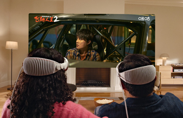 两个人头戴 Apple Vision Pro，并排坐在沙发上观看电影《飞驰人生 2》。