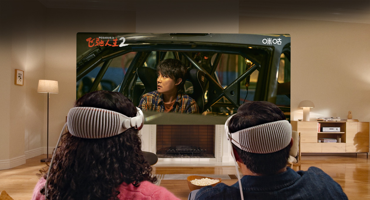 两个人头戴 Apple Vision Pro，并排坐在沙发上观看电影《飞驰人生 2》。