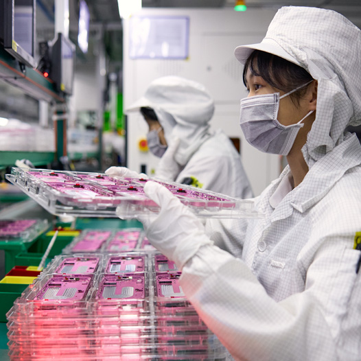 两名穿着全罩式工作服的员工在组装厂处理 iPhone 部件