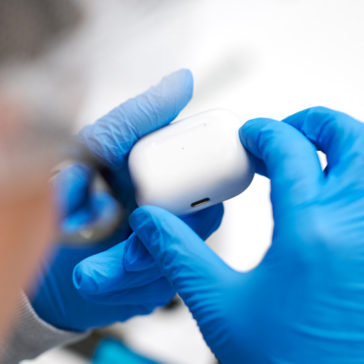 戴着乳胶手套的双手拿着 AirPods 充电盒