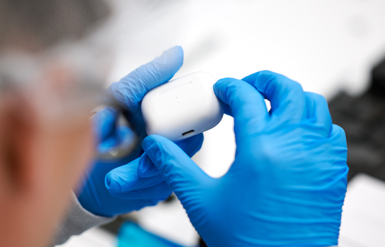 戴着乳胶手套的双手拿着 AirPods 充电盒